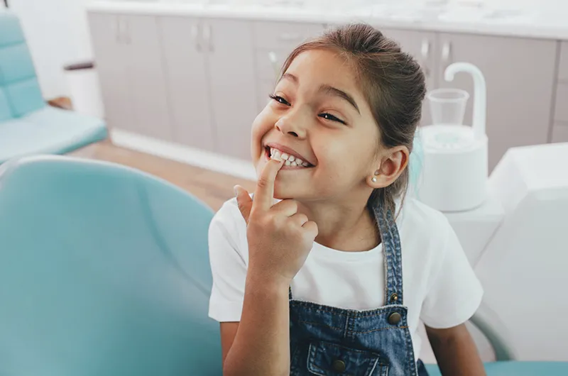 Kind lächelt und zeigt mit Finger auf Zahn